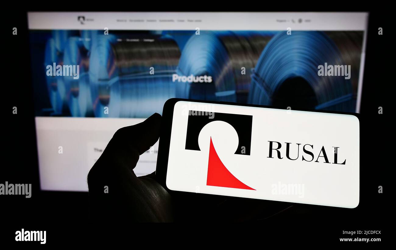 Person holding cellphone with logo of Russian company United Company RUSAL IPJSC on screen in front of business webpage. Focus on phone display. Stock Photo