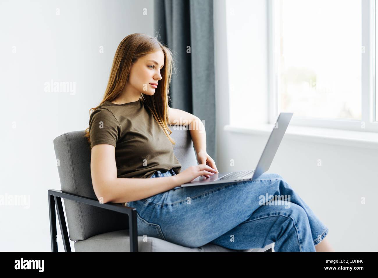 Young woman sitting on chair with laptop Stock Photo - Alamy