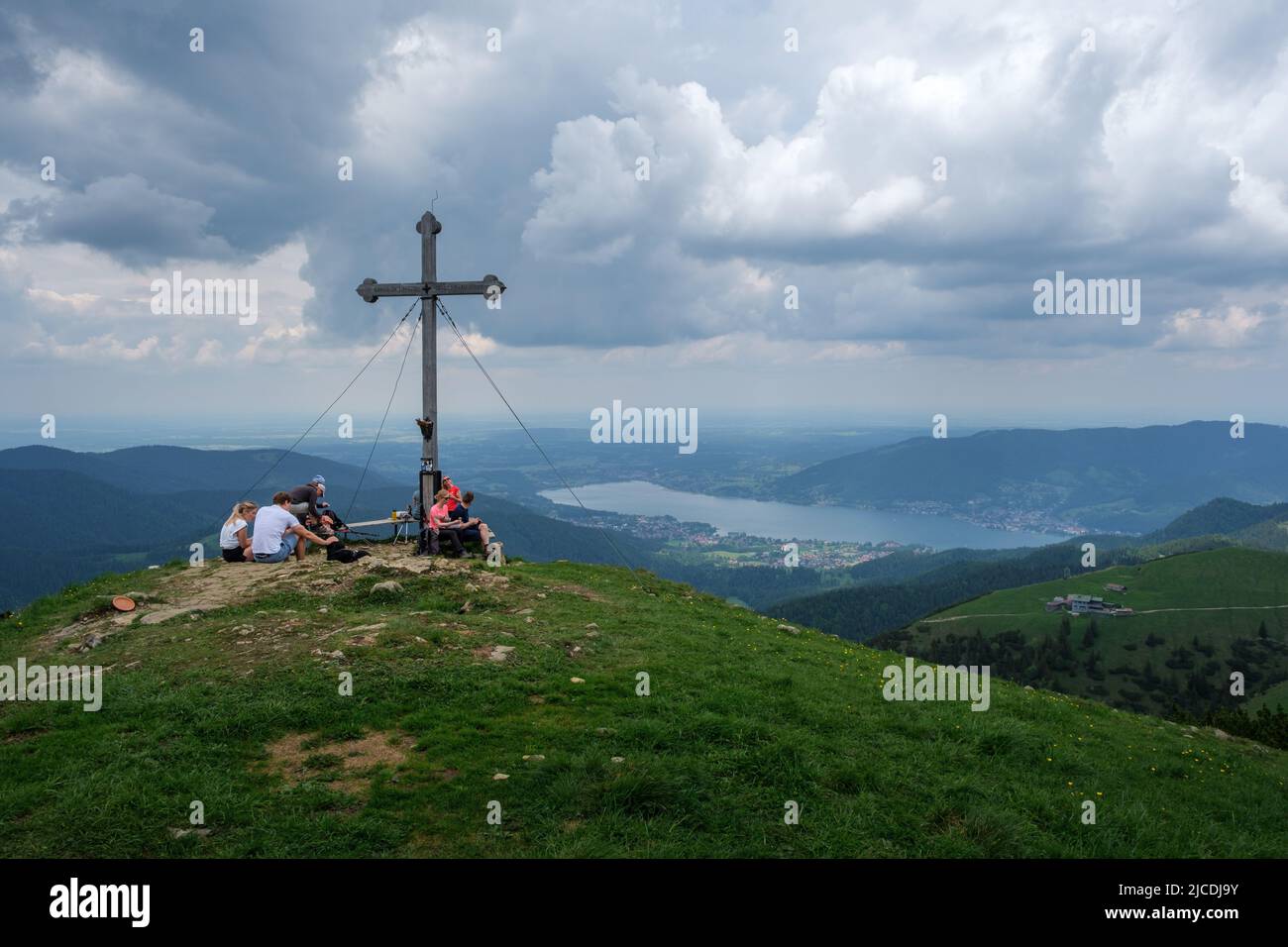 Different hiker at the summit cross from the bavarian summit Hirschberg with view to the lake Tegernsee. Stock Photo