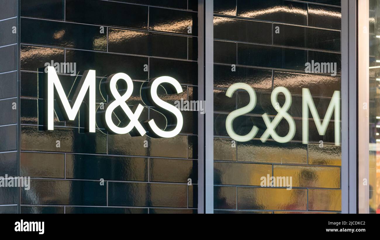 Marks & Spencer, Manchester Market Street, England, UK. M&S logo sign on dark tile wall reflected in store window. Premium homeware, clothing and food Stock Photo