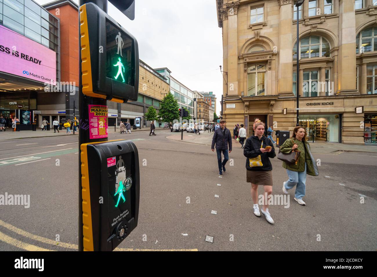 Pedestrians crossing the road at Market Street, Manchester. A puffin crossing displays the 'green man' as people cross the road. England, UK Stock Photo