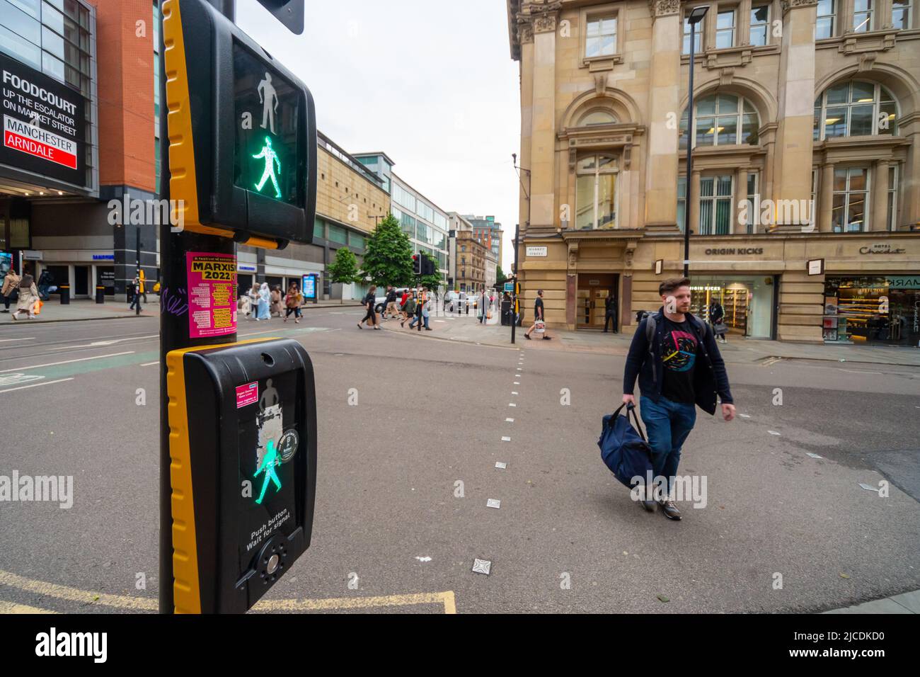 Pedestrian crossing the road at Market Street, Manchester. A puffin crossing displays the 'green man' as someone crosses the road. England, UK Stock Photo