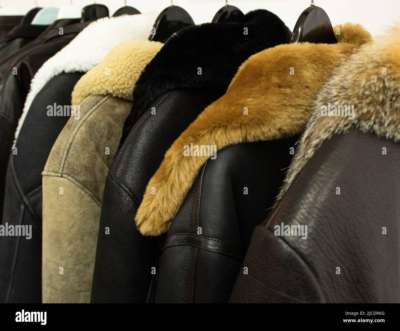 Collection of leather jackets on hangers in the shop. Many new men's winter jackets with fur. Background and closeup texture of leather, Stock Photo