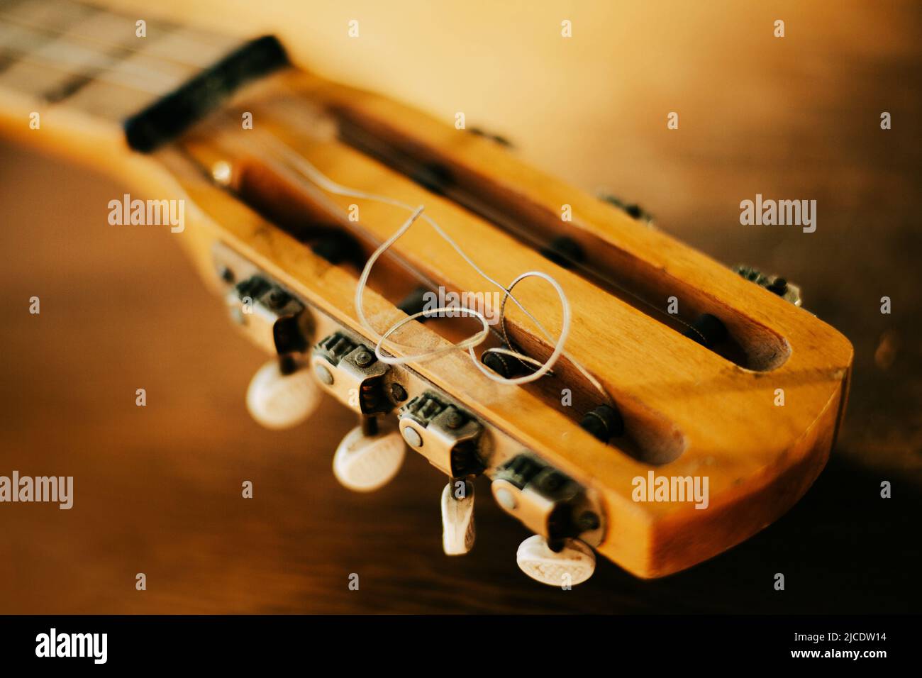 The neck of an old wooden six-string acoustic guitar with metal strings, illuminated by sunlight. Music lessons. Creation. Stock Photo