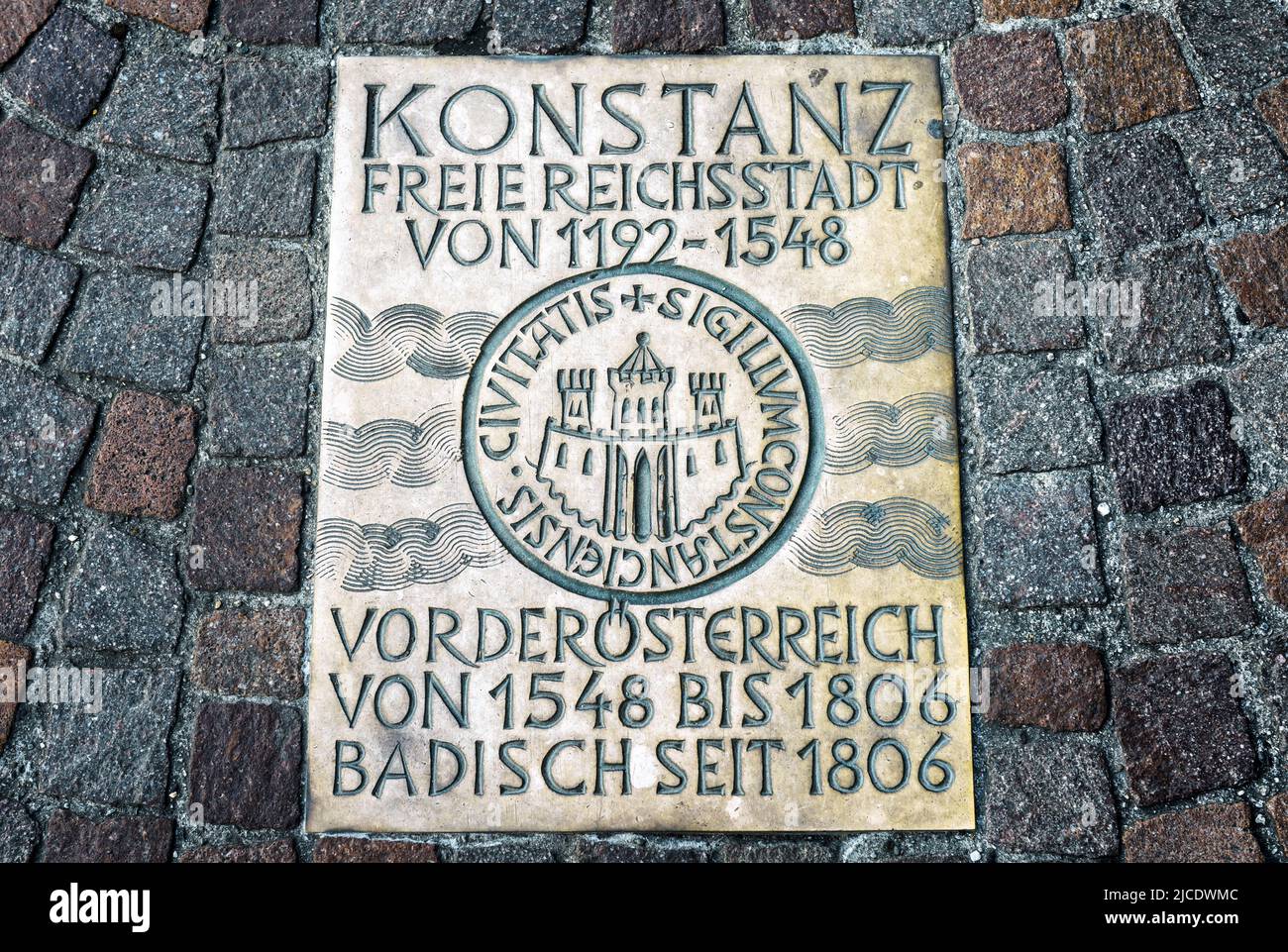 Cobblestone pavement in Constance (Konstanz), Germany. Metal plate on road in old town of Constance. Translation: Constance is free city from 1192, pa Stock Photo