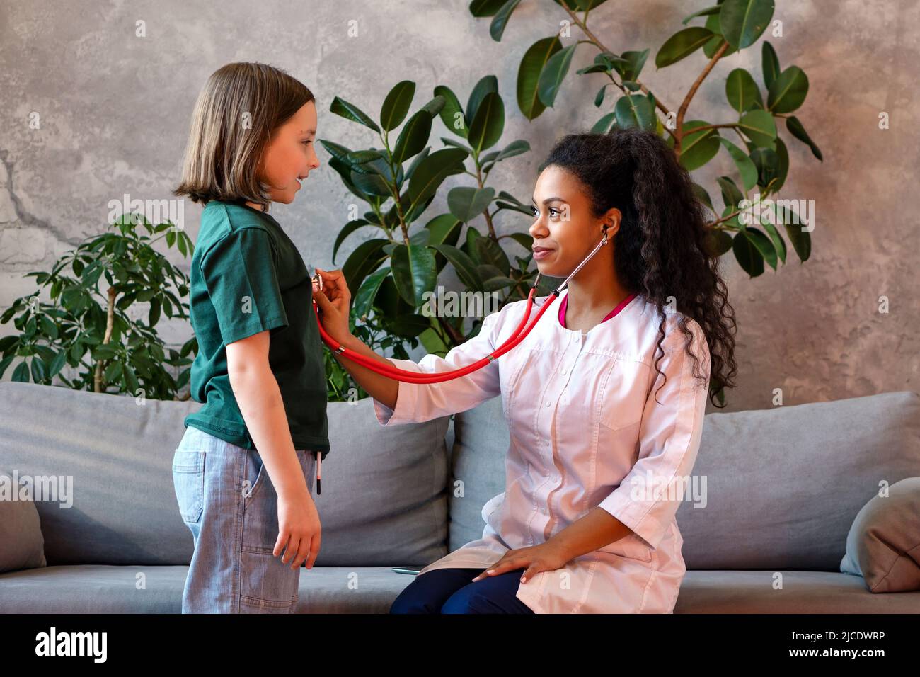 Auscultation Heart and Lungs Exam with Stethoscope. Child Girl Visiting Doctor for regular checkup. African American Female Pediatrician in Pediatric Stock Photo