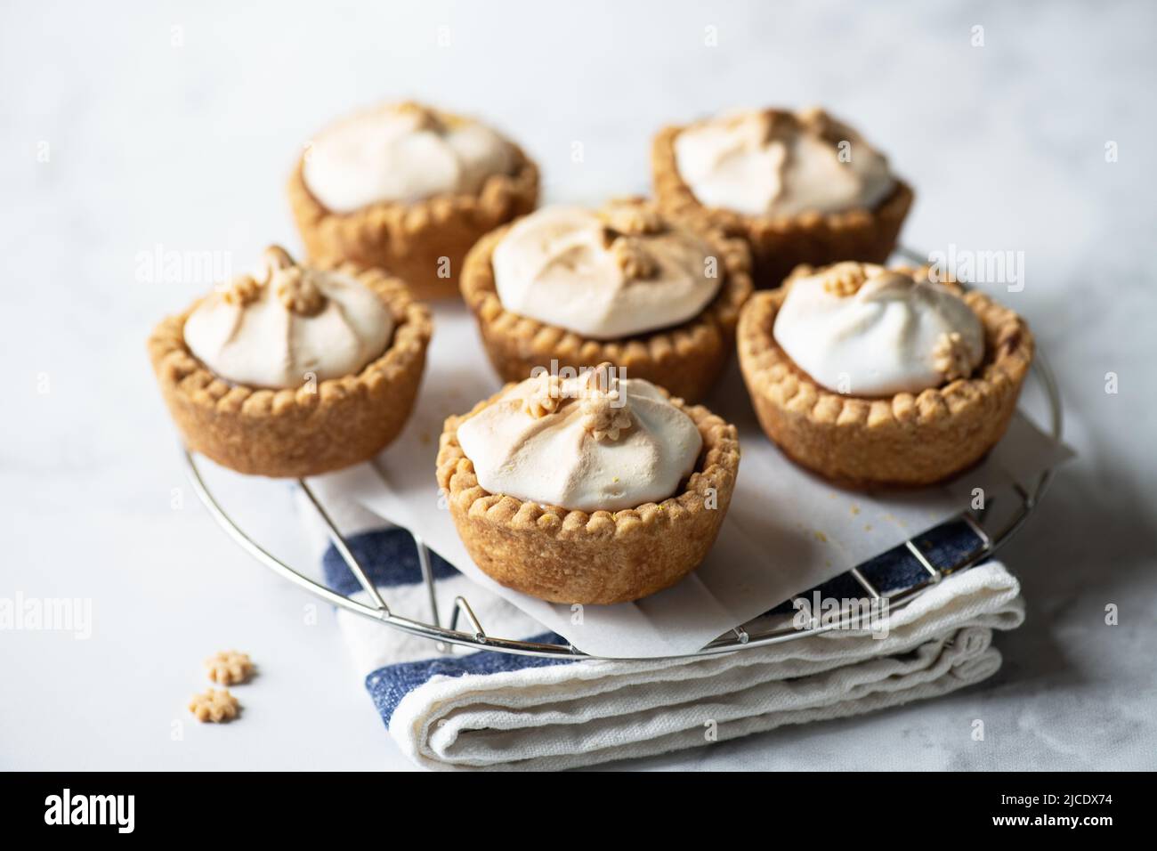Lemon curd tartlets with whipped meringue on a wire rack on a gray background. Stock Photo