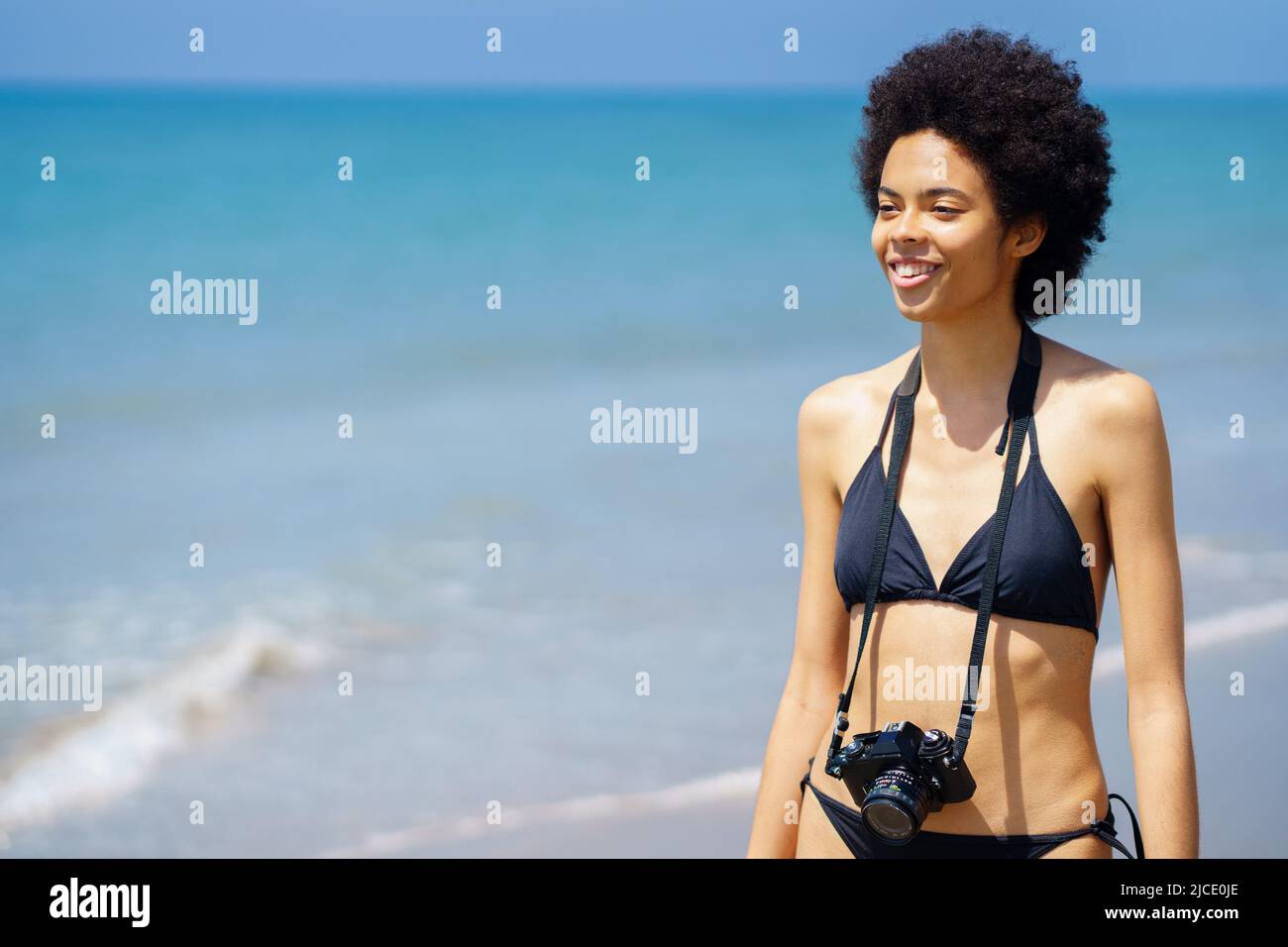 Smiling black woman with photo camera near sea Stock Photo