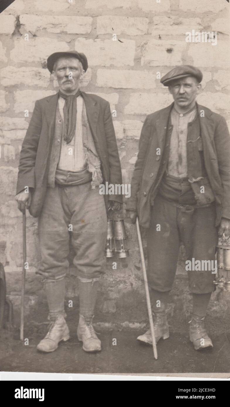 Photograph of two miners carrying safety lamps and sticks, early 20th century. They are wearing flat caps, waistcoats and jackets, trousers tucked into socks and sturdy boots. One also has a neckerchief Stock Photo