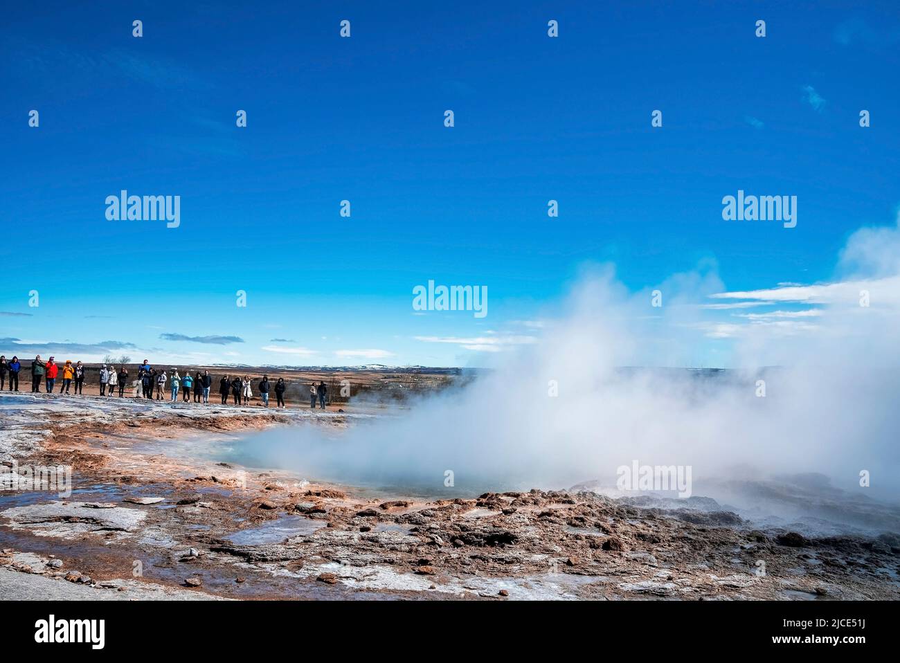 Tourists exploring Strokkur geyser eruption in valley against blue sky ...
