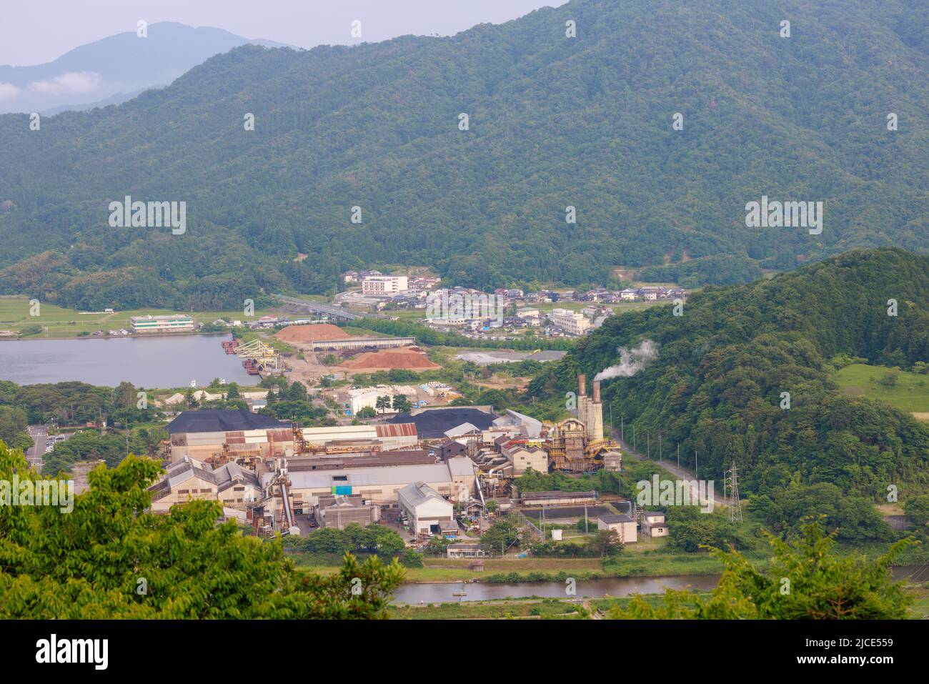 Smoke stack billows from small factory in rural mountain landscape Stock Photo