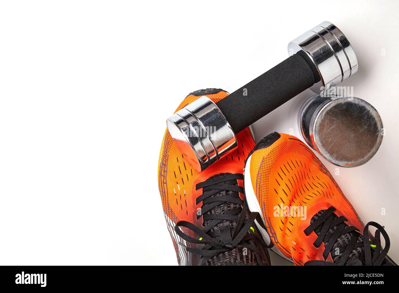 Metallic heavy dumbbell dropped on leg in orange sneaker. Strength