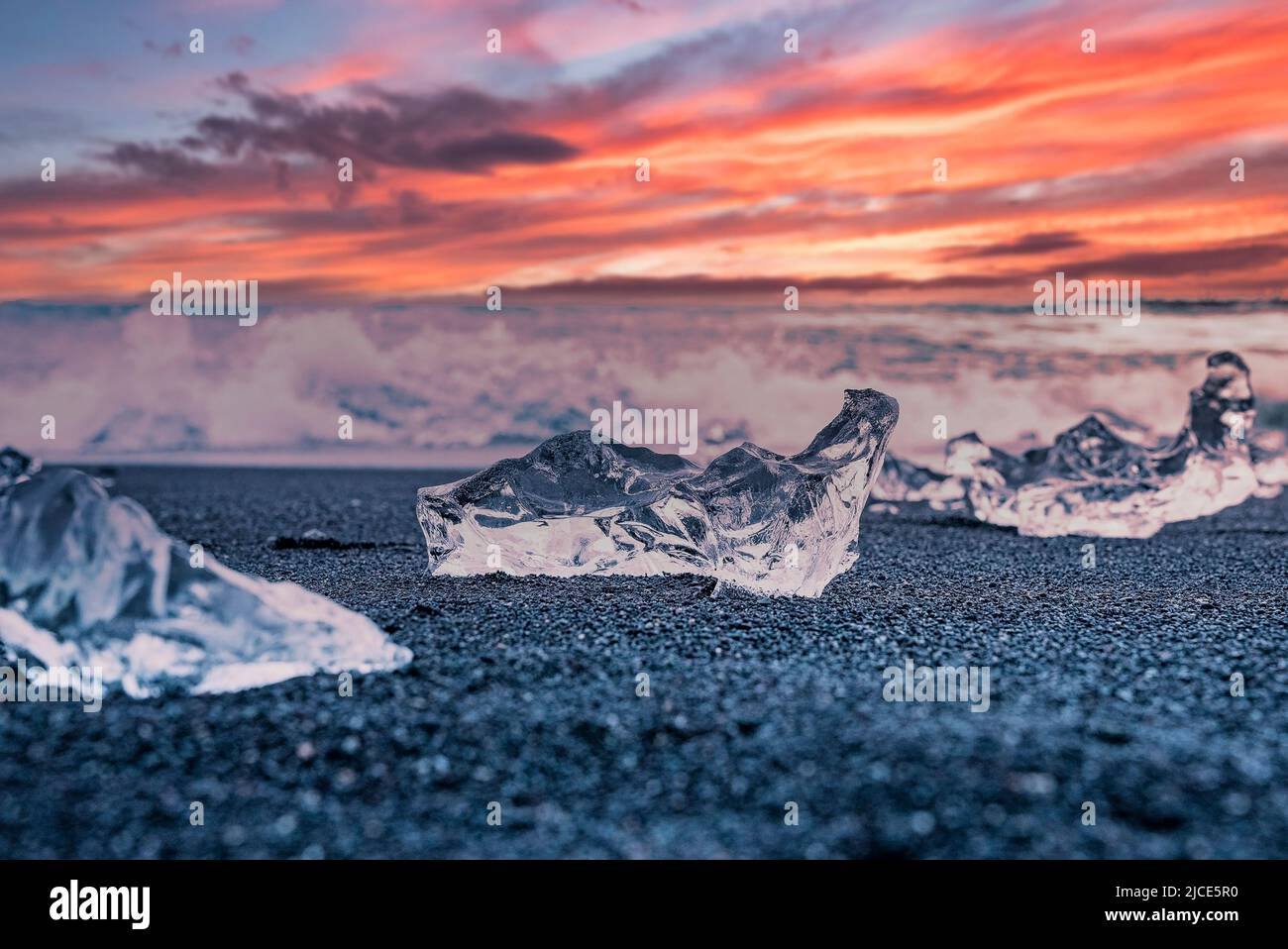 Iceberg chunk on black sand at Diamond beach against dramatic sky during sunset Stock Photo