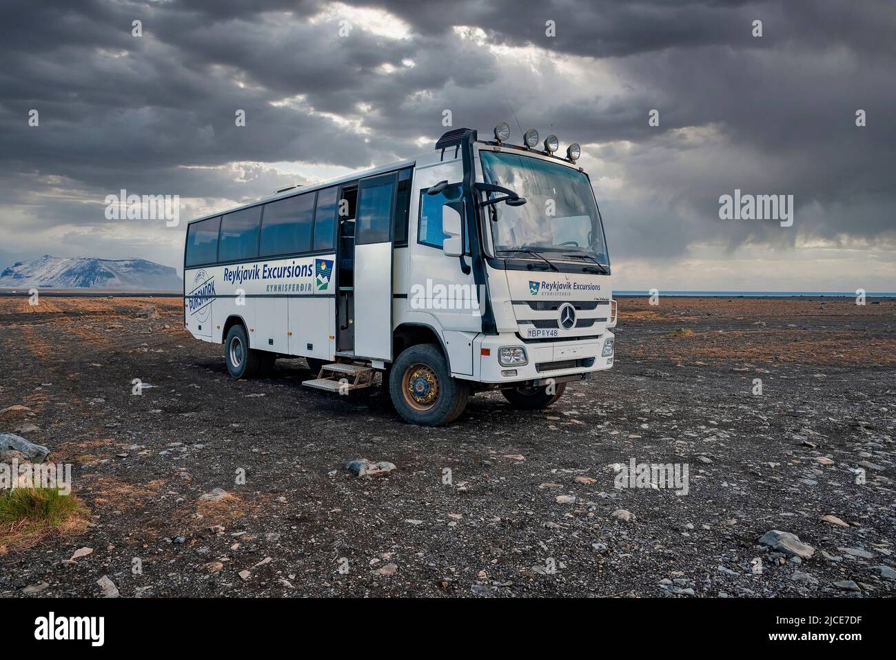 Reykjavik Excursions bus parked on lava sand at Highland against cloudy sky Stock Photo