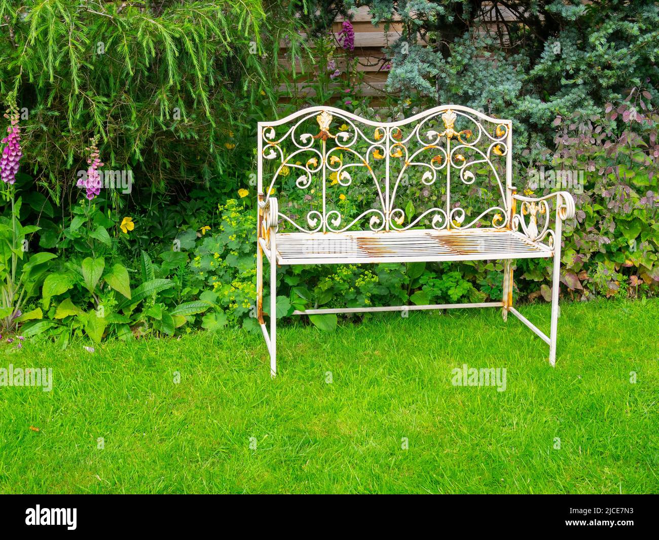 A yellow painted wrought iron garden bench seat in a sunny corner of a domestic garden Stock Photo