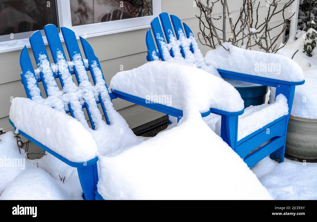 two blue Adrirondack chairs in a a back yard covered in snow Stock Photo