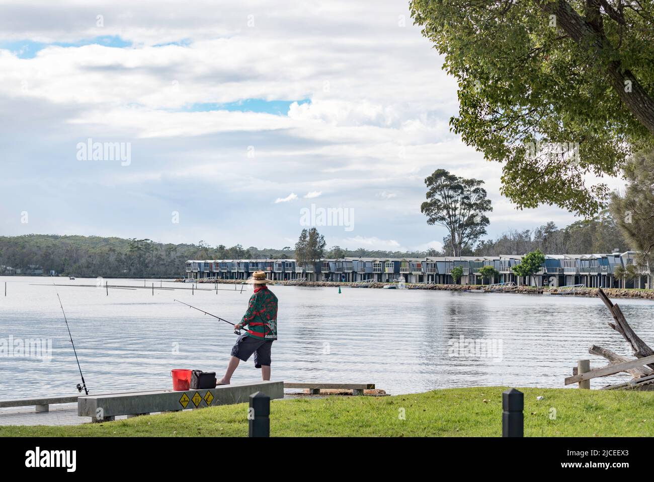 A man fishes from a wharf near Holiday cabins built along the water's edge of Lake Conjola on the New South Wales, South Coast of Australia Stock Photo