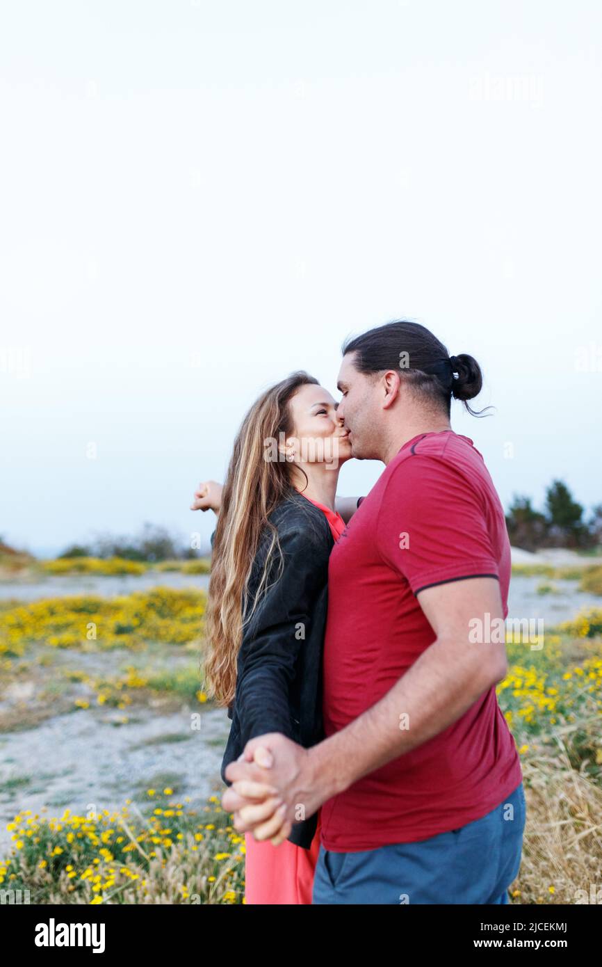 Portrait of lovely middle-aged couple kissing and hugging while standing on grass in summer park. Stock Photo