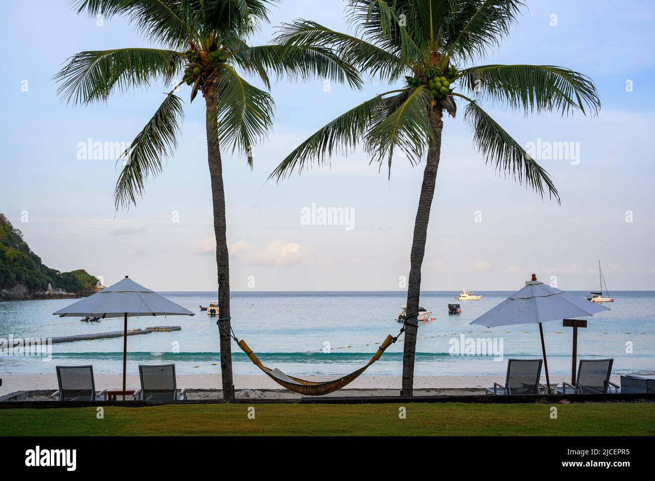 A pair of coconut trees with a cradle tied in the middle. and a beach chair in the morning, looking like a happy smiling face, at the seaside of an is Stock Photo