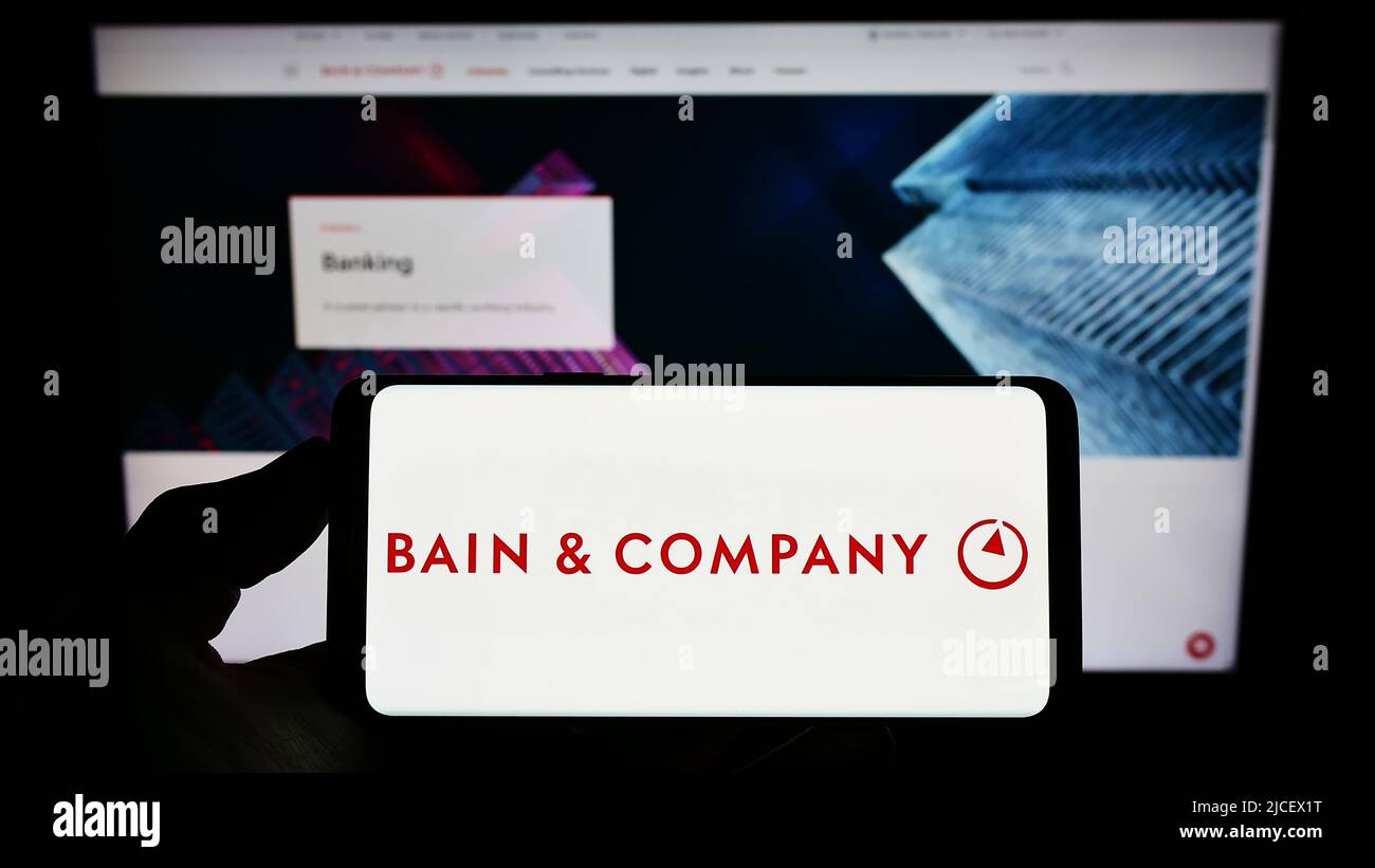 Person holding smartphone with logo of US consulting company Bain and Company Inc. on screen in front of website. Focus on phone display. Stock Photo