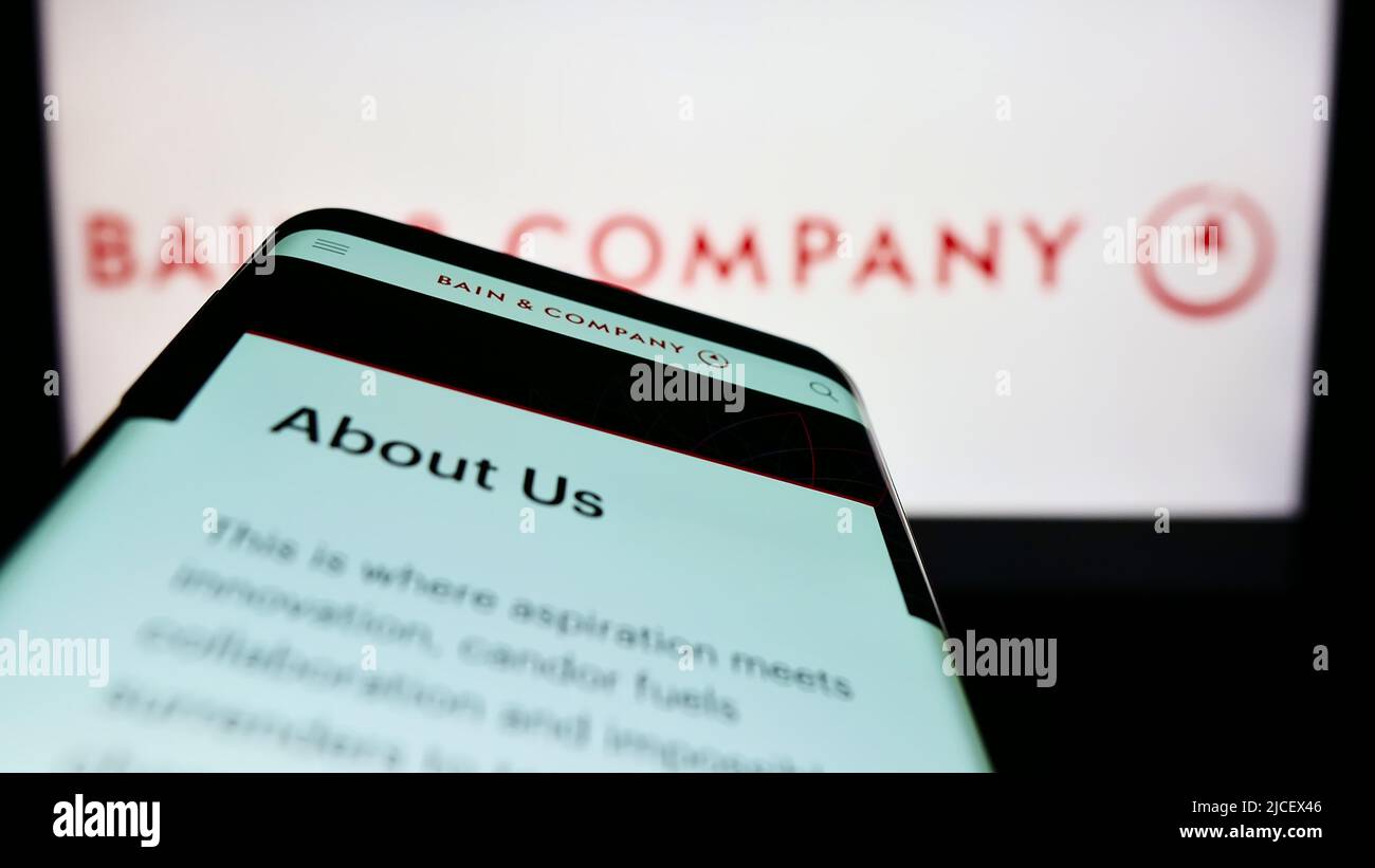 Smartphone with website of US consulting company Bain and Company Inc. on screen in front of business logo. Focus on top-left of phone display. Stock Photo