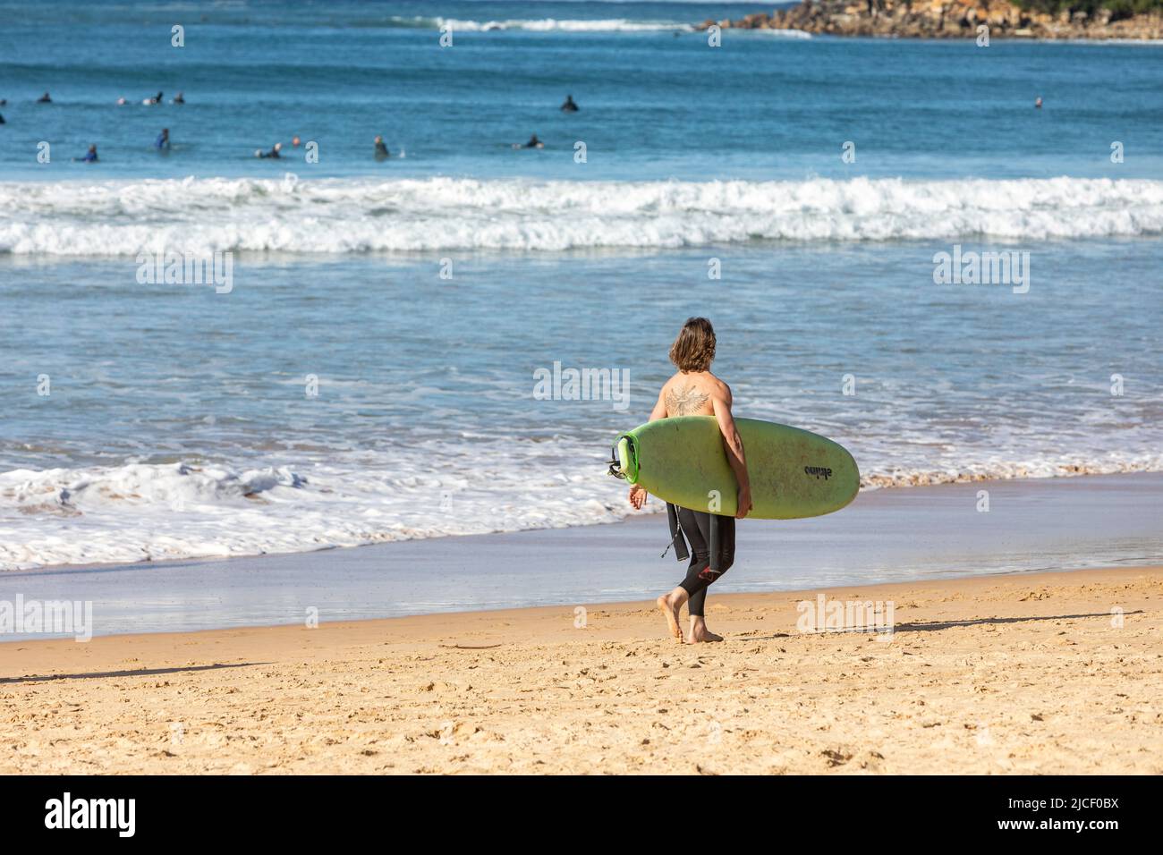 Australian male surfer, with back tattoo, carries surfboard along Manly Beach Sydney on a winters day,Australia Stock Photo