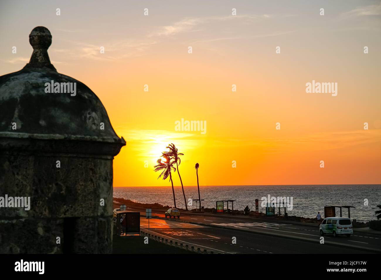 Beautiful sunset sky over the sea with palm trees and building in front of the city wall, Cartagena, Colombia Stock Photo