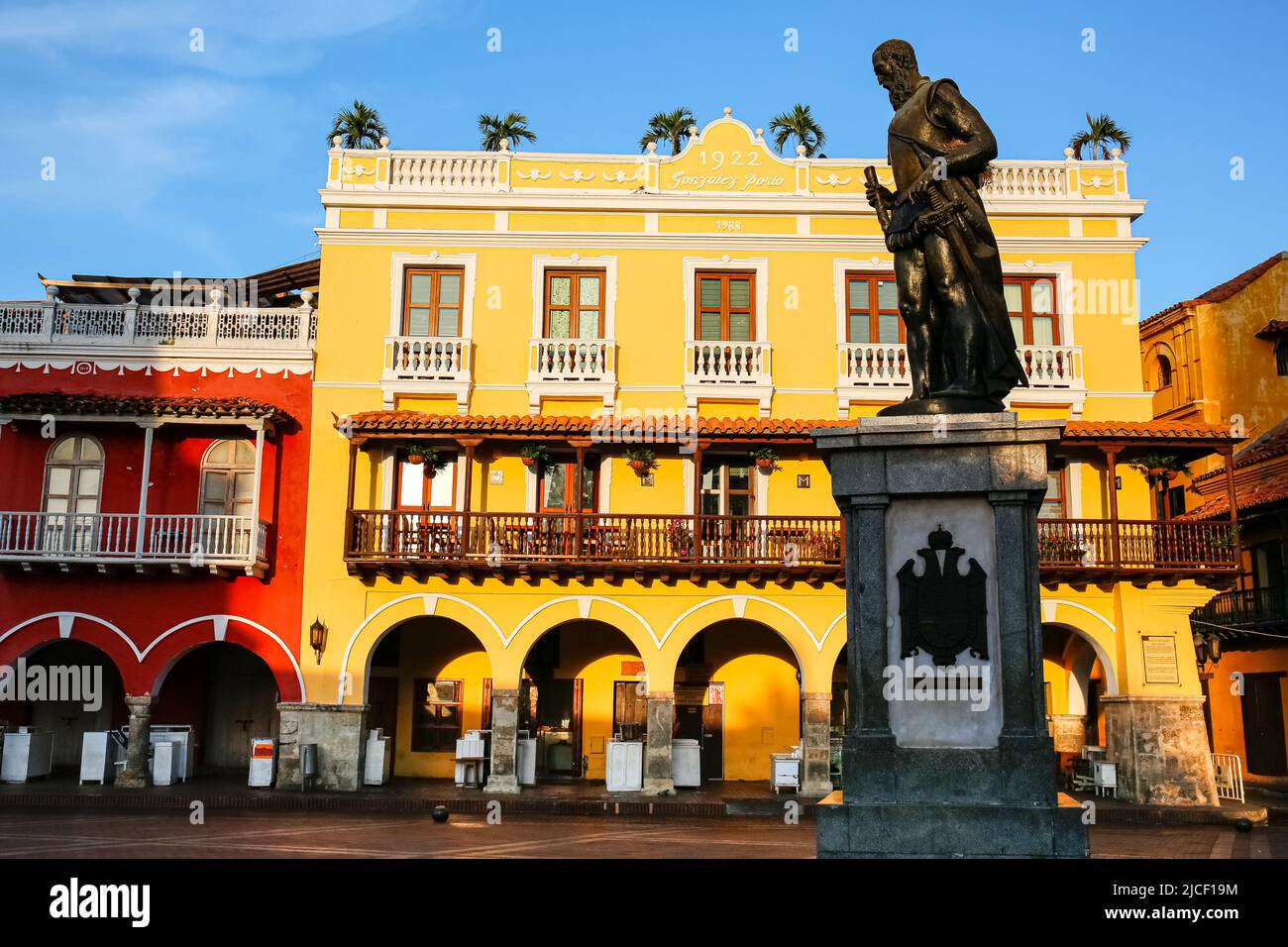 Colorful historic buildings at Plaza de los Cochem (Carriages square) on a sunny day in Cartagena with statue in the shadow Stock Photo