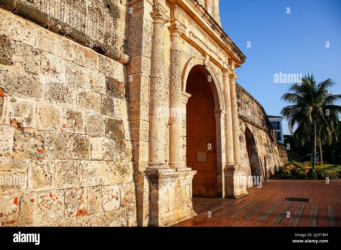 View to an ancient wall and entrance gate in sunshine, palm tree in background, Cartagena, Colombia, Unesco World Heritage Stock Photo