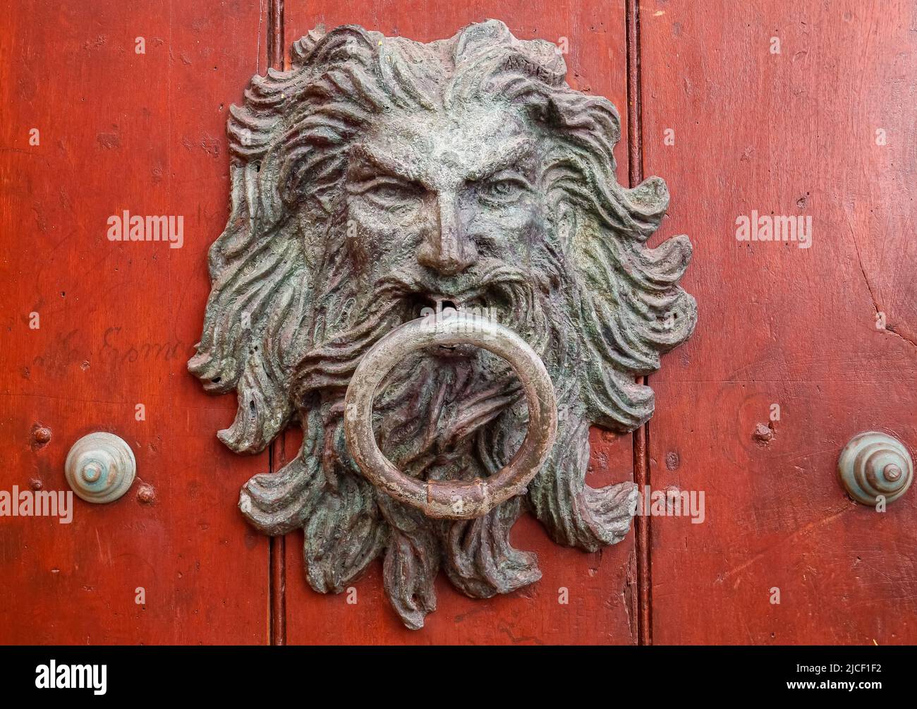 Artful door knocker with face and ring on a reddish-brown wooden door in Cartagena, Colombia, Unesco World Heritage Stock Photo