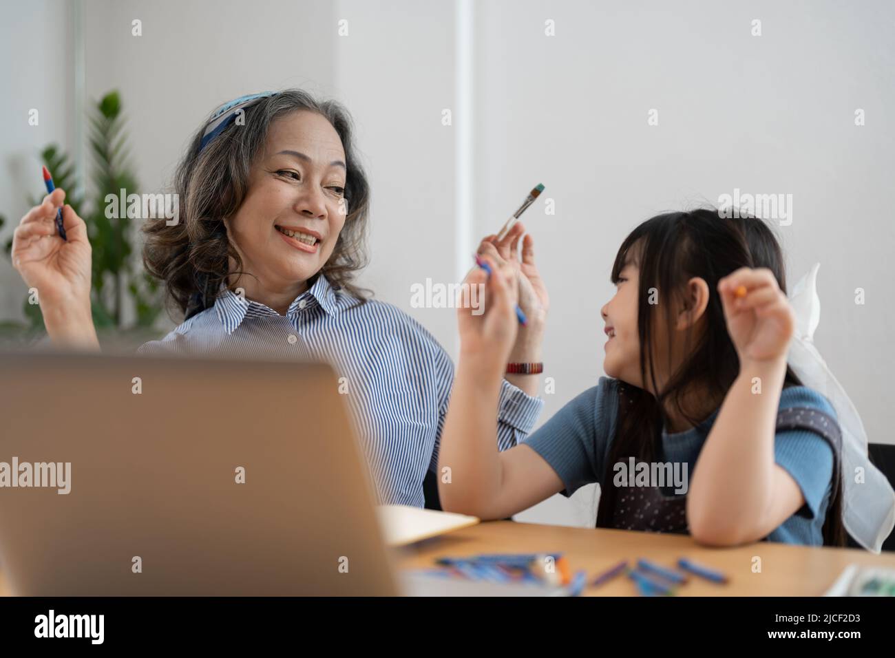 Happy senior grandma and cute little kid granddaughter watching cartoons on laptop together, happy older grandmother grawing and painting. Stock Photo