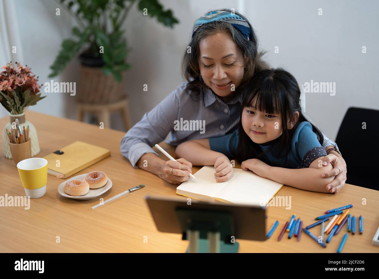 Smiling senior grandma and cute little kid granddaughter watching cartoons on laptop together, happy older grandmother grawing and painting. Stock Photo