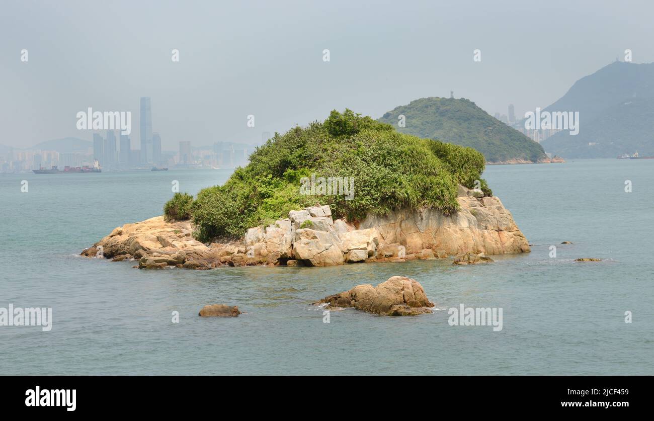 ICC tower rising behind the rocky coastline of Peng Chau island in Hong Kong. Stock Photo