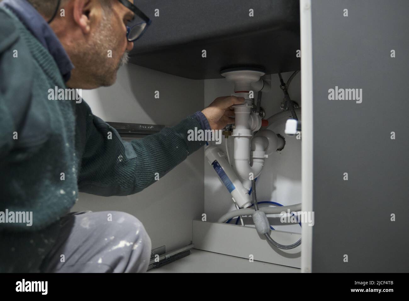 Mature plumber installing sink siphon in domestic kitchen Stock Photo