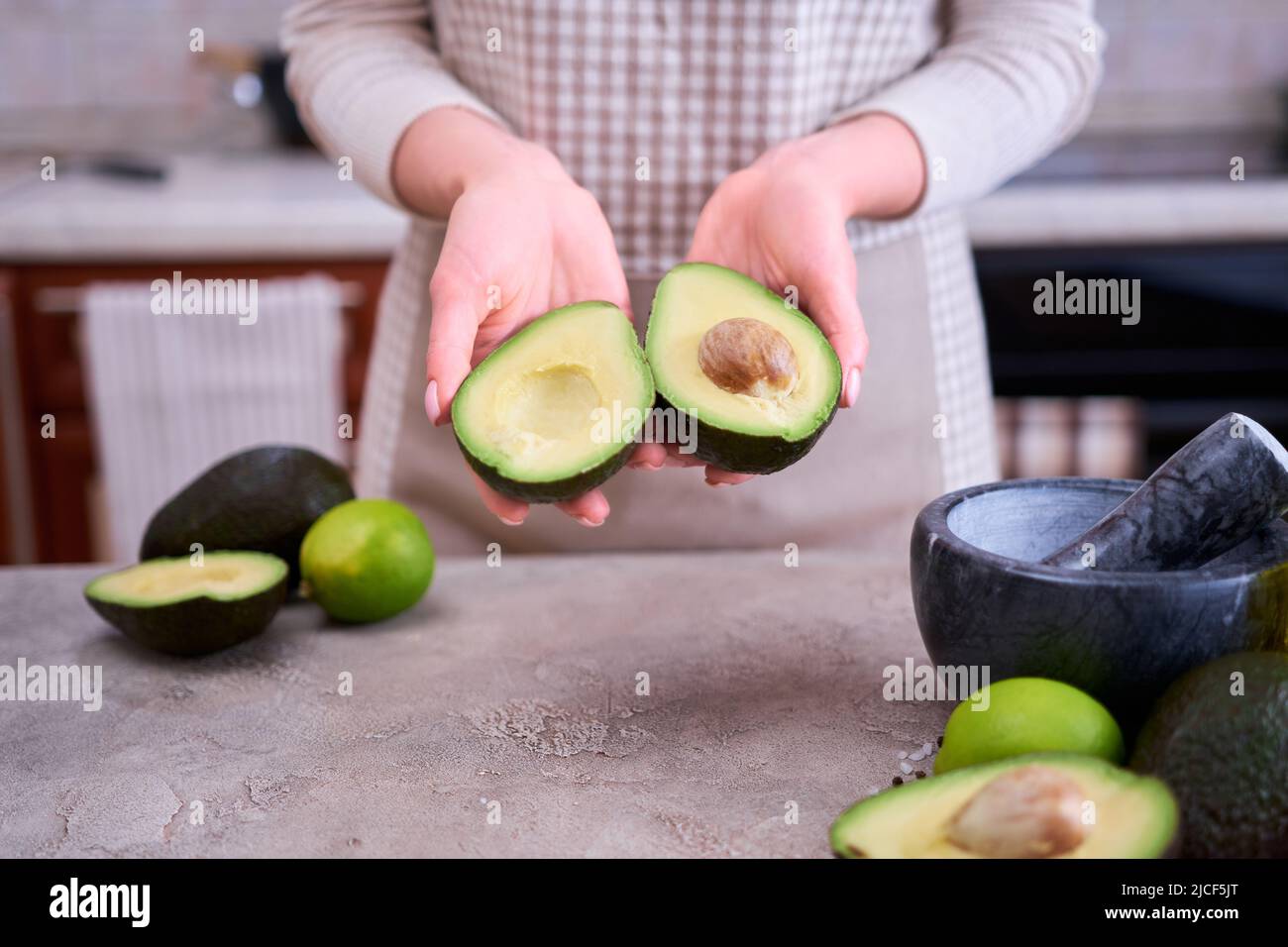 Closeup on hands holding fresh avocado cut in half over grey concrete ...