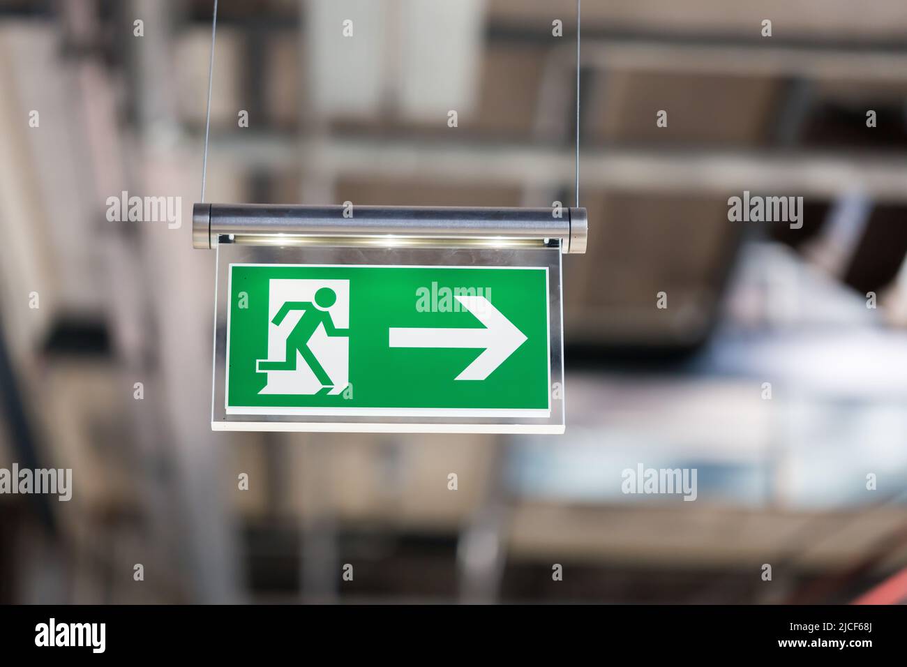 Essen, Germany - Mar 26, 2022: Illuminated emergency exit sign, hanging from the ceiling. With running figure and an arrow which points to the right. Stock Photo
