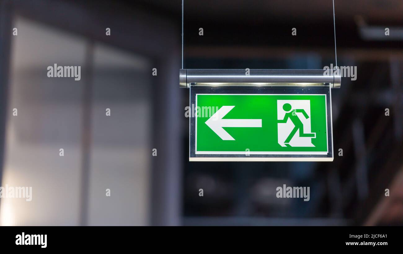 Essen, Germany - Mar 26, 2022: Illuminated emergency exit sign. Arrow pointing to the left. Stock Photo