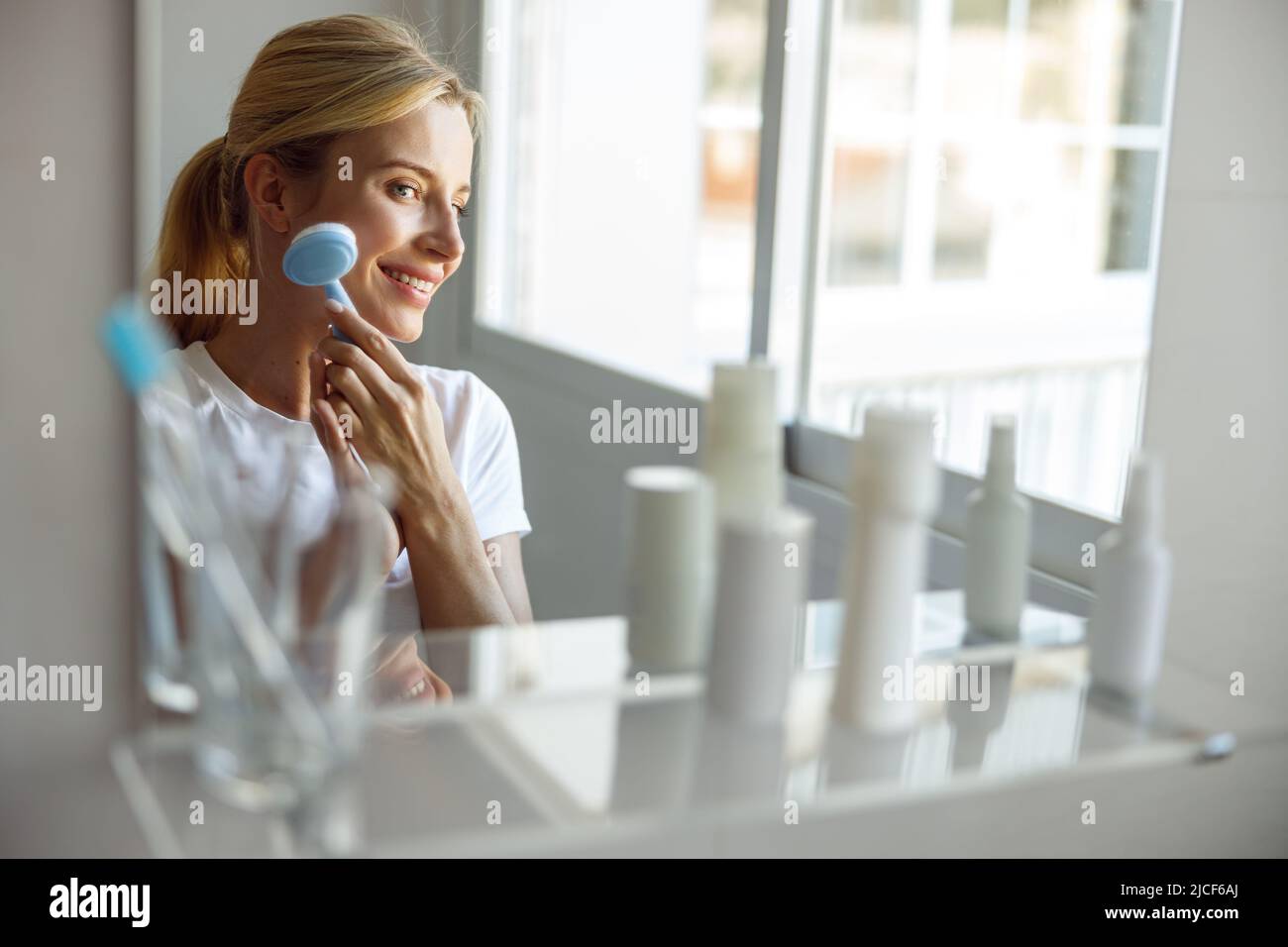 Cheerful happy young female smiling and massaging cheek with brush massager. Stock Photo