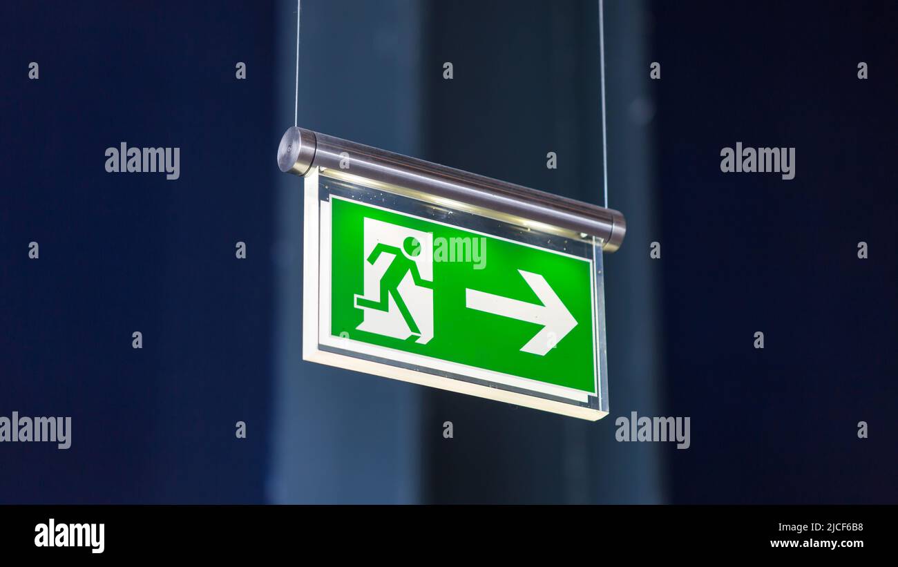 Essen, Germany - Mar 26, 2022: Emergency exit sign. With running figure, arrow pointing to the right. Blurry background. Stock Photo