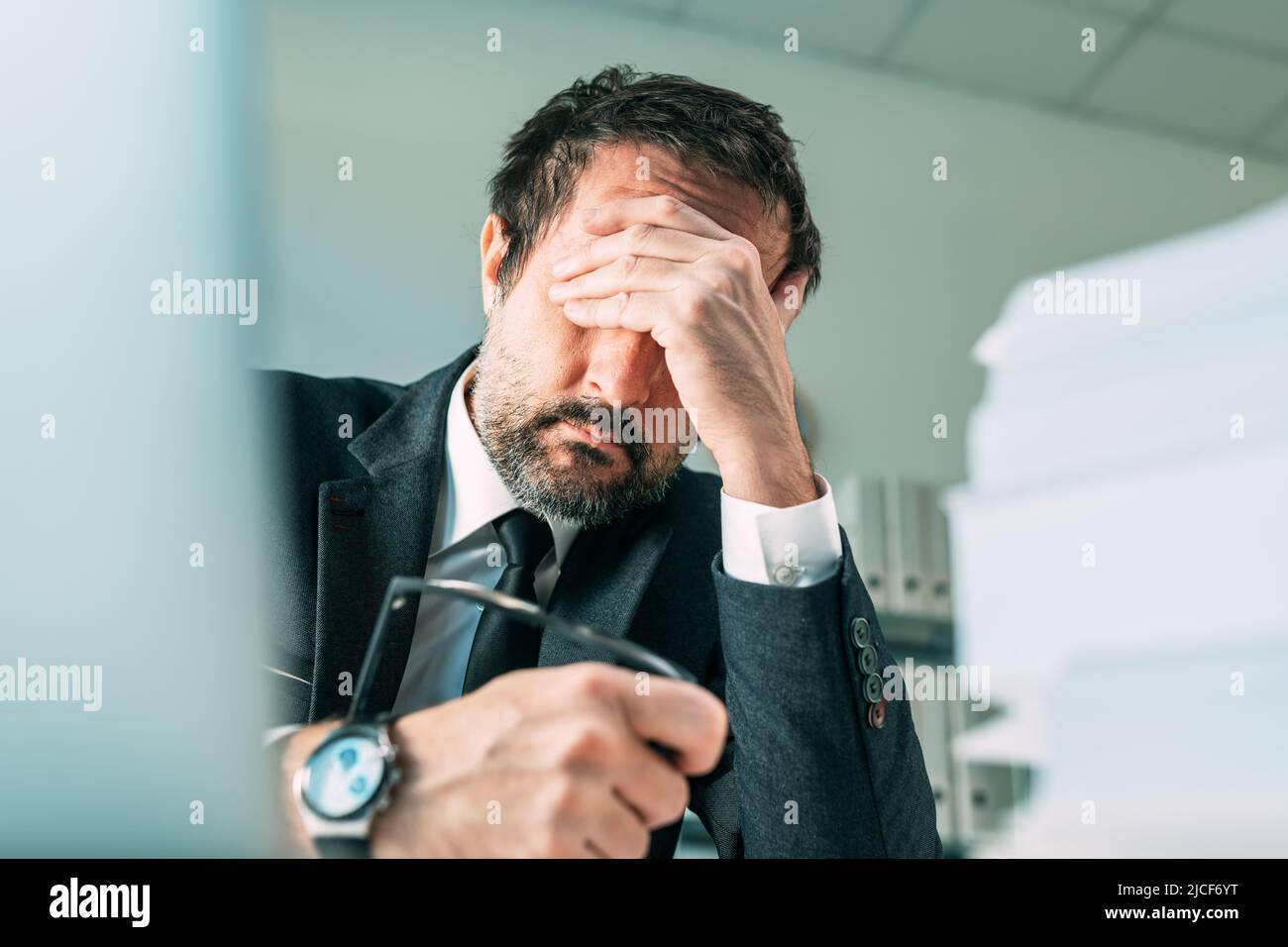 Overworked businessman at office desk, tired fatigued business owner in stressful situation, selective focus Stock Photo