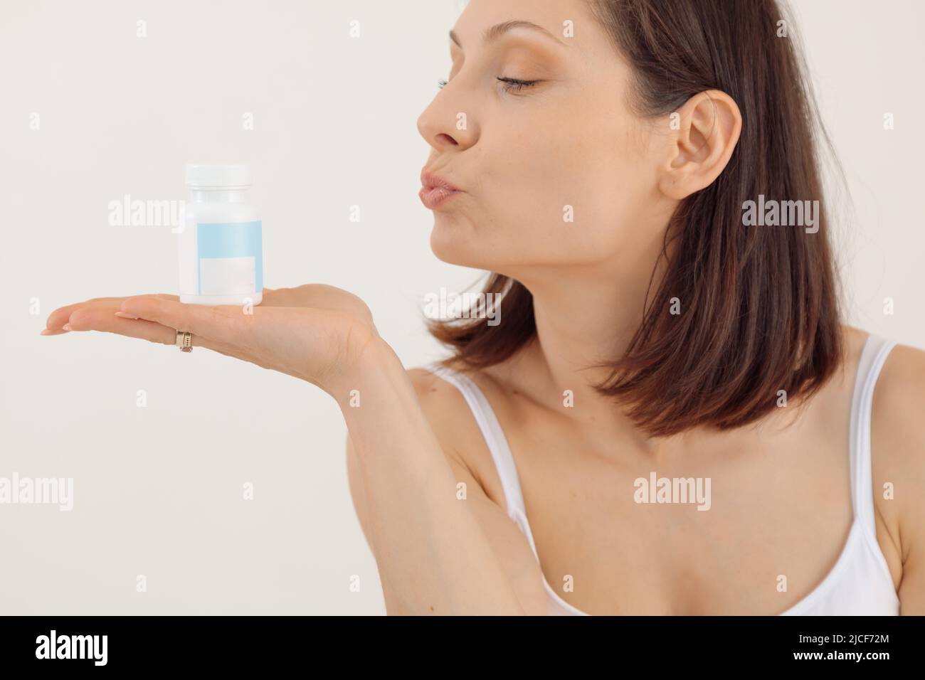 Portrait of young woman with short dark hair wearing white top, holding blue plastic bottle of pills for womans health. Stock Photo
