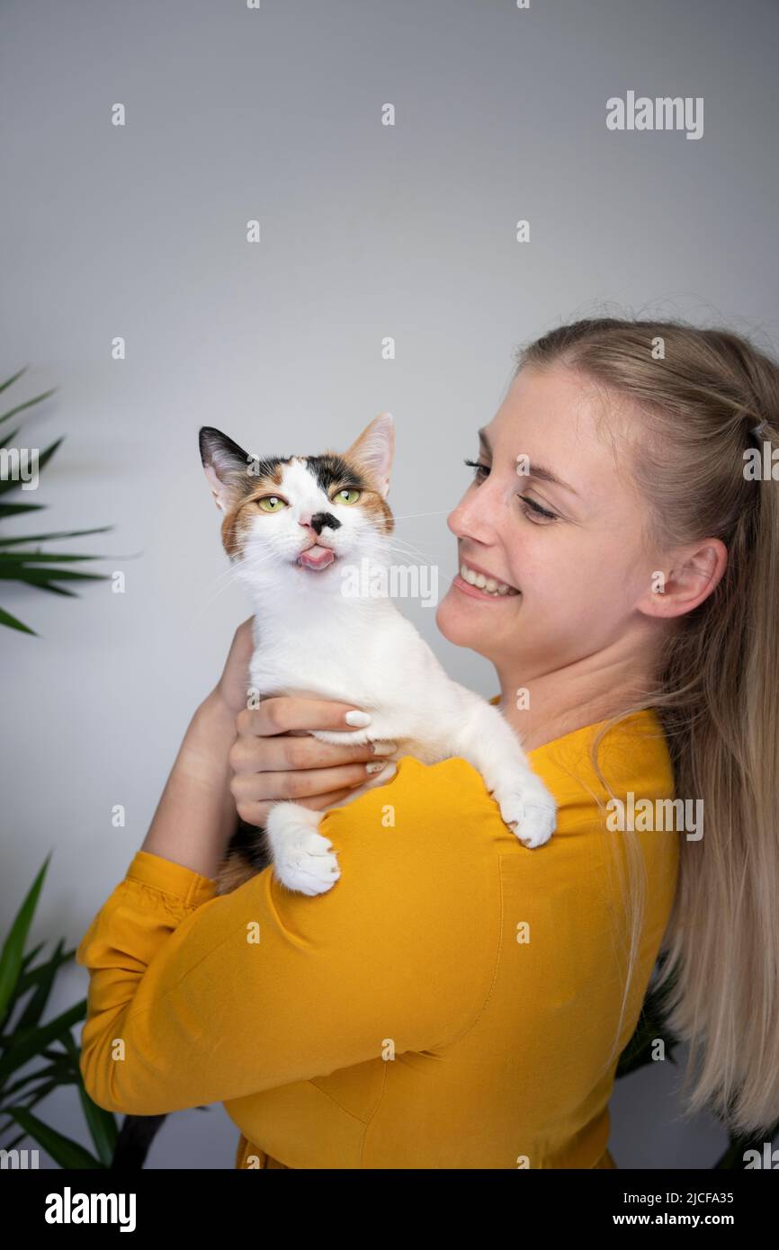 young blond woman carrying her naughty cat that is sticking out tongue looking at camera Stock Photo