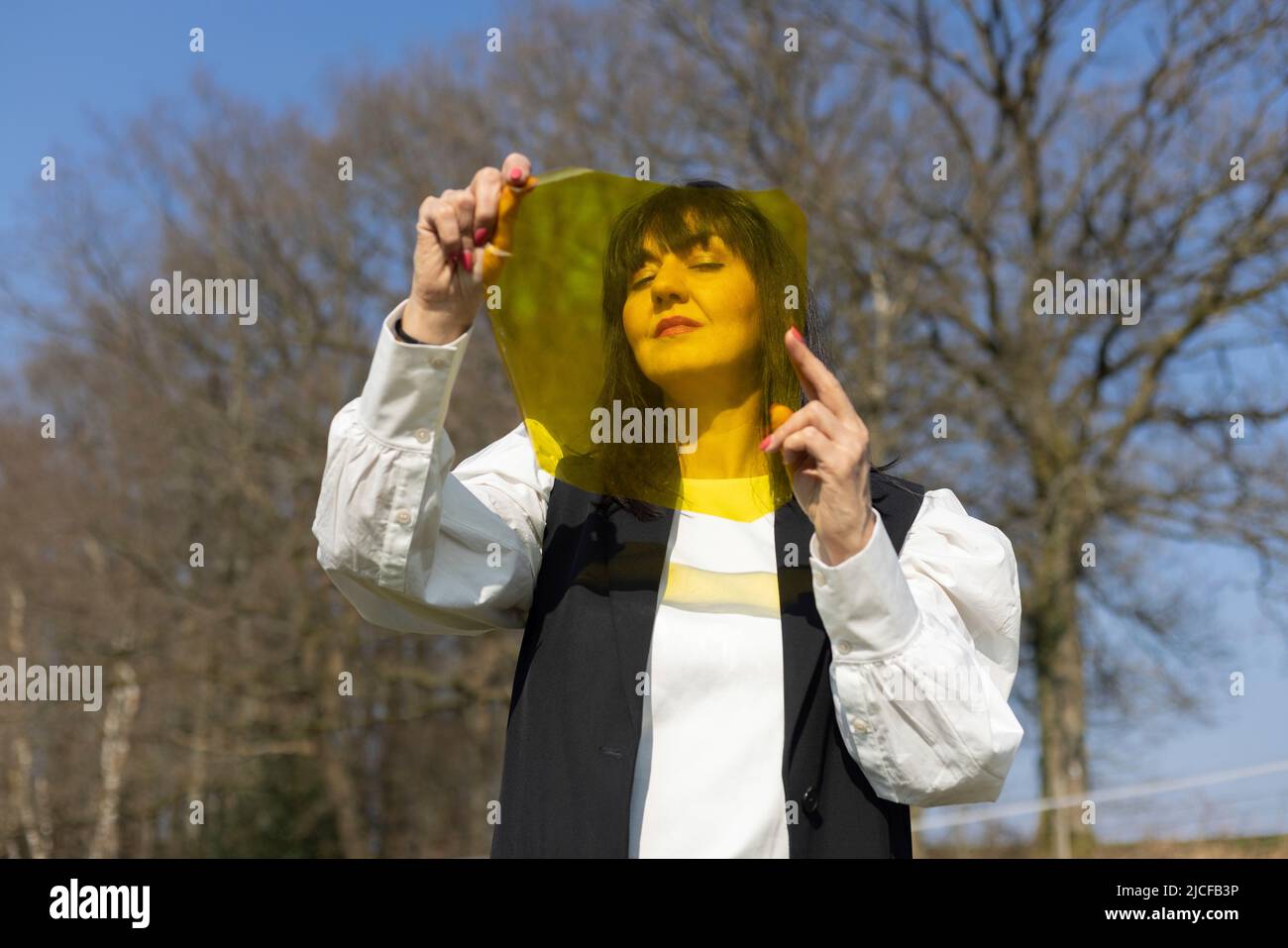 Black haired woman looking through yellow color film Stock Photo