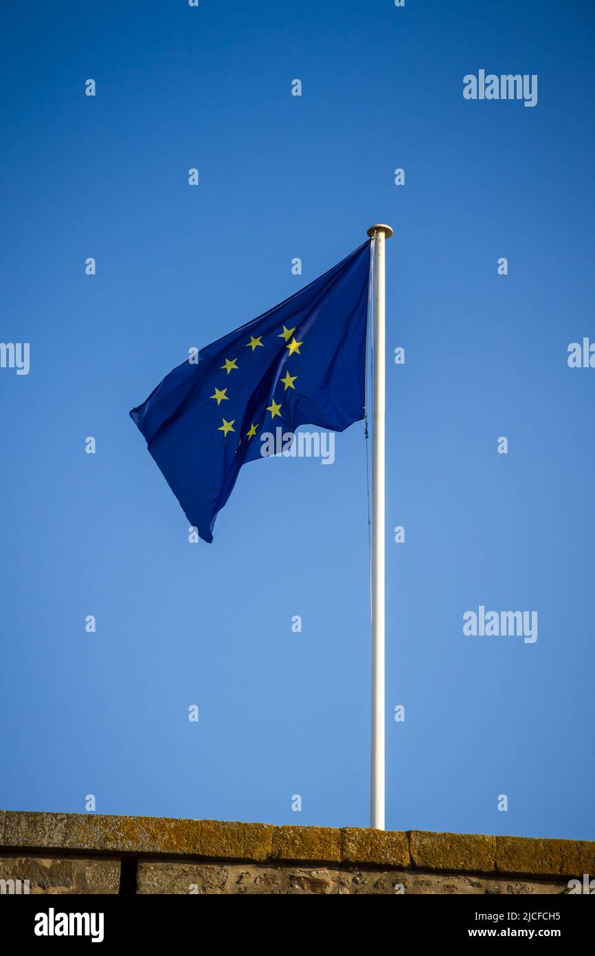 European Union flag on a pole floating in the wind. Blue sky background ...