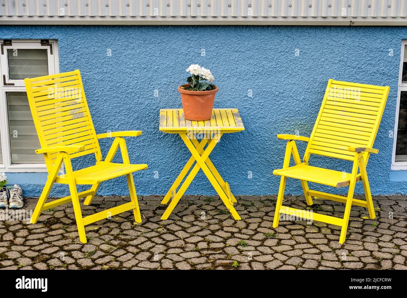 Stykkisholmur, Iceland, May 3, 2022: two yellow wooden chairs and ditto table on a terrace in front of the wooden plaster facade of a house Stock Photo