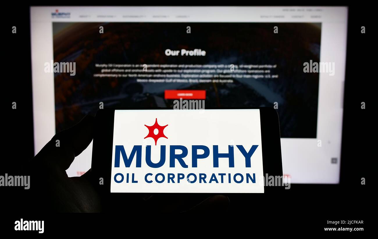 Person holding smartphone with logo of US exploration company Murphy Oil Corporation on screen in front of website. Focus on phone display. Stock Photo