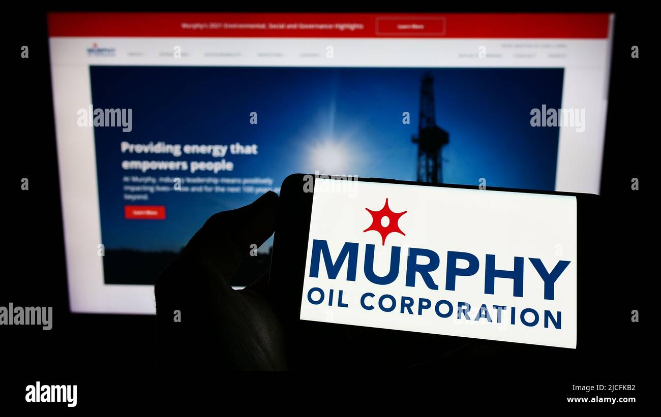 Person holding cellphone with logo of American exploration company Murphy Oil Corporation on screen in front of webpage. Focus on phone display. Stock Photo