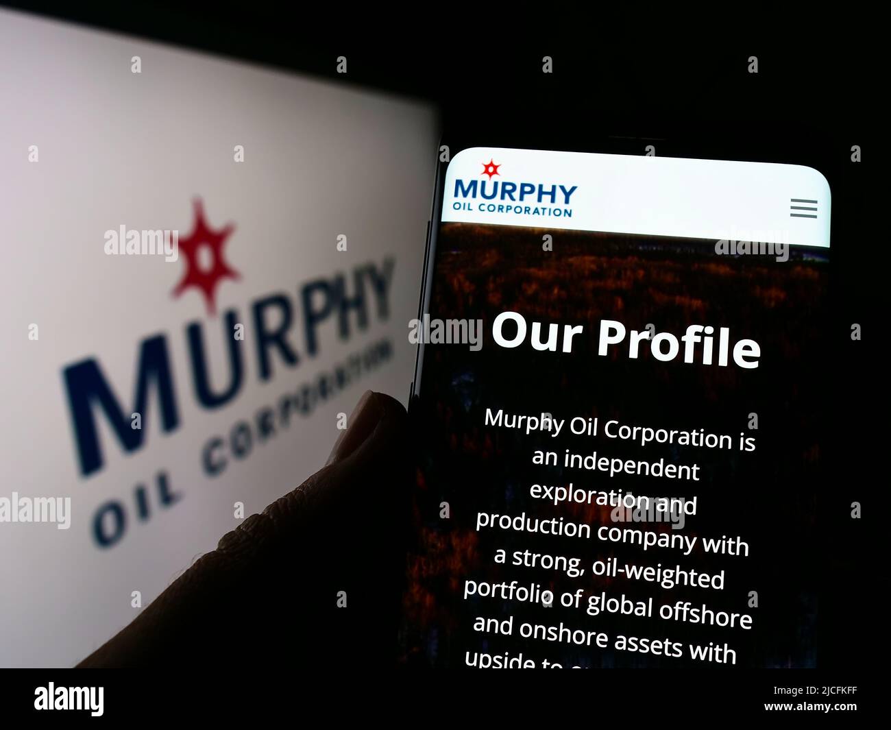 Person holding cellphone with webpage of US exploration company Murphy Oil Corporation on screen with logo. Focus on center of phone display. Stock Photo