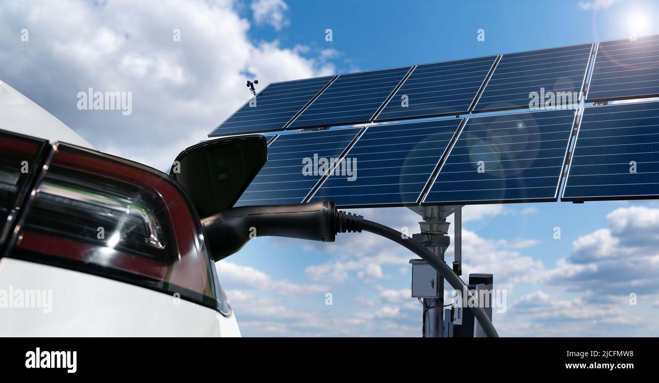 Close up of electric car with a connected charging cable on the background of solar panel - source of clean renewable energy Stock Photo
