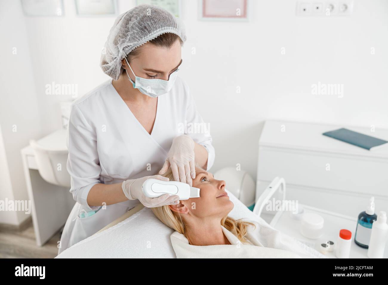 Female cosmetologist working using ultrasonic face scrubber performing